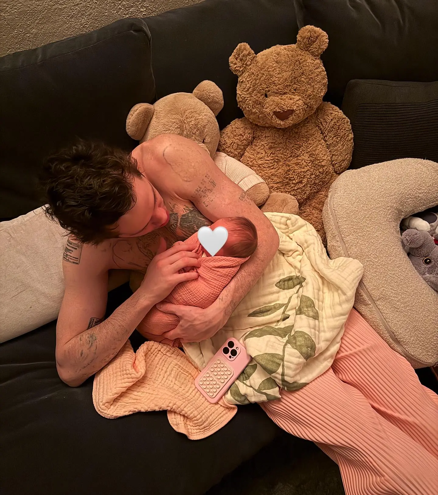 Pete Davidson cradling a newborn on a sofa with teddy bears.