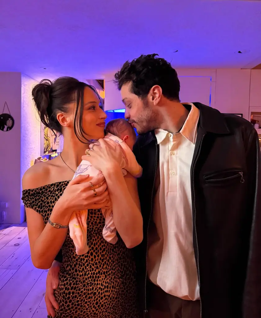 Pete Davidson kissing a baby held by a woman in a leopard print dress.