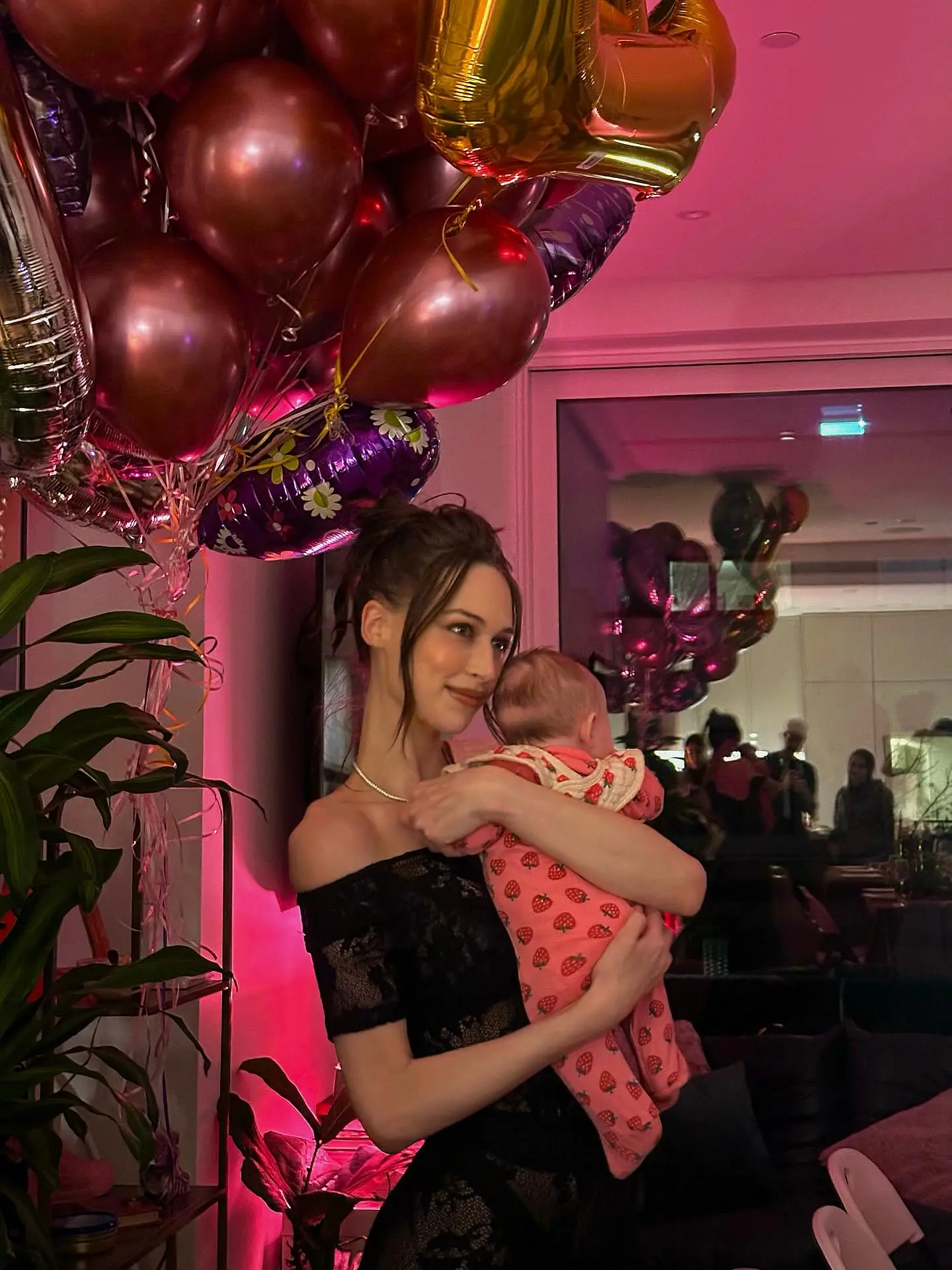 Elsie Hewitt holding a baby, surrounded by balloons, with pink lighting