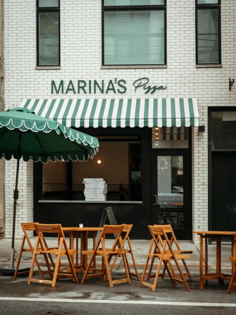 Exterior of Marina's Pizza shop with green and white striped awning and outdoor seating.