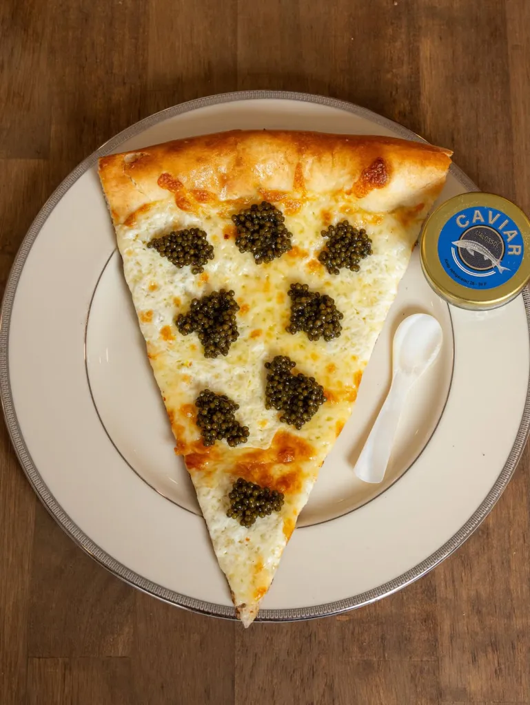 A slice of cheese pizza topped with dollops of caviar, next to a jar of caviar and a small spoon.