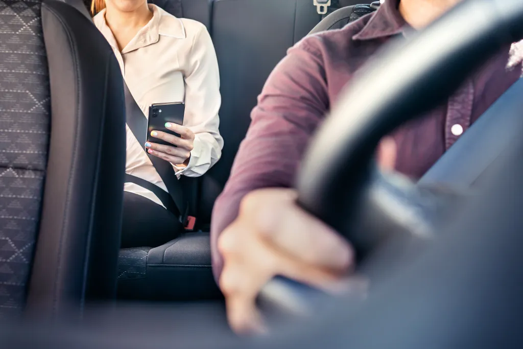 stock image of person on a phone in the back seat with a driver at the wheel