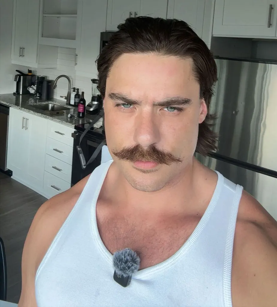 Dalton Eatherly, also known as ChudtheBuilder, wearing a white tank top and a mustache with a lavalier microphone clipped to his shirt.