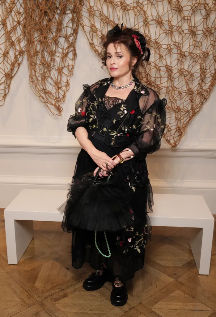 Helena Bonham Carter in an embroidered black tulle outfit and a jeweled necklace, holding glasses and a purse.