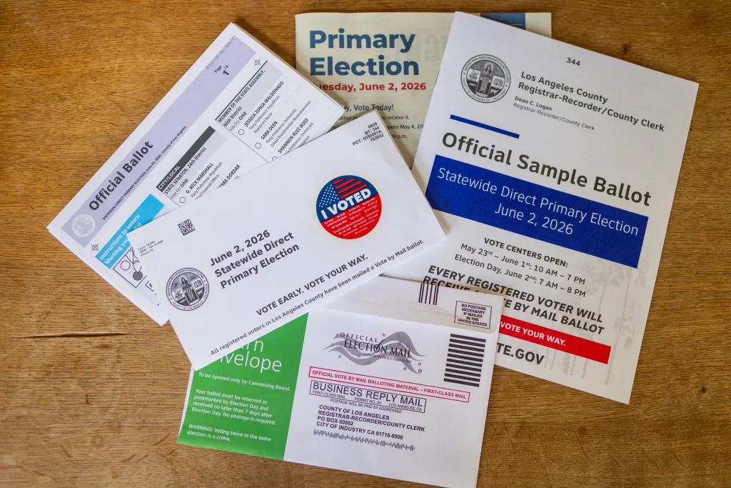 Photo illustration of election voting materials, including an official ballot, sample ballot, and mail-in envelopes.