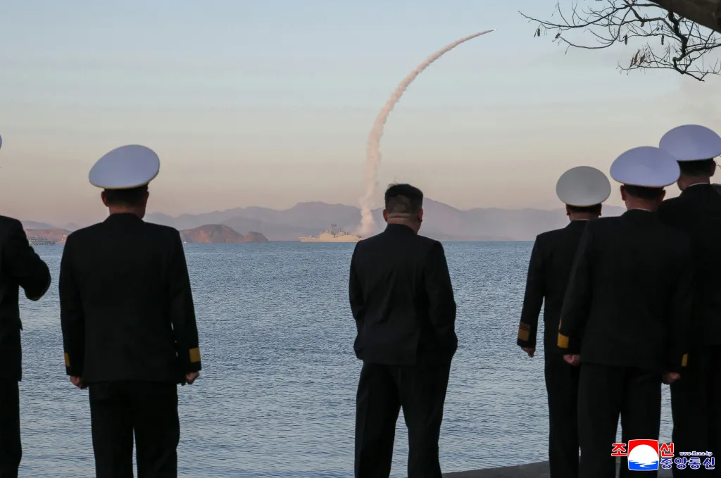 Kim Jong Un, surrounded by officers, watches a missile launch from a destroyer.