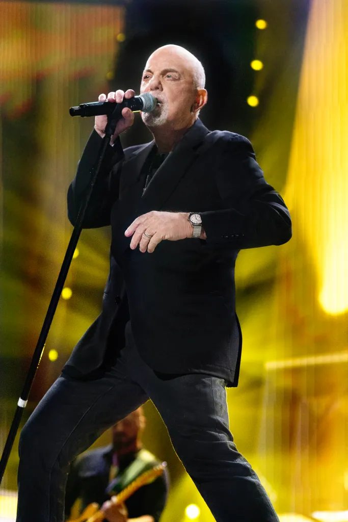 Billy Joel performing on stage, holding a microphone.