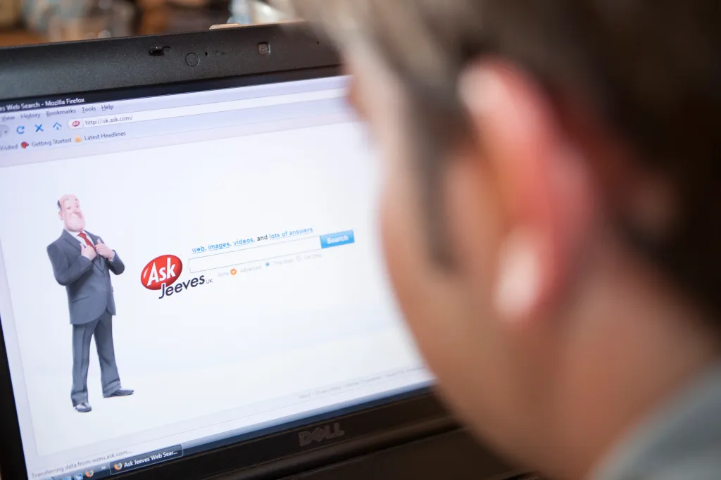 A person looking at a laptop screen displaying the Ask Jeeves website.