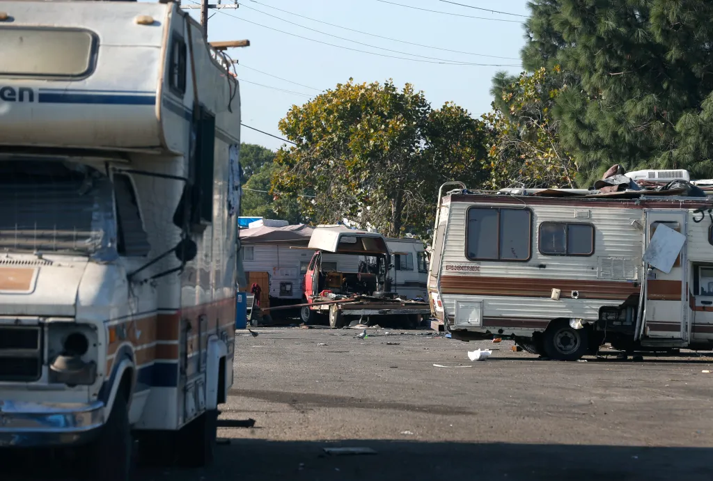 Recreational vehicles are parked at a homeless encampment with trash and debris.