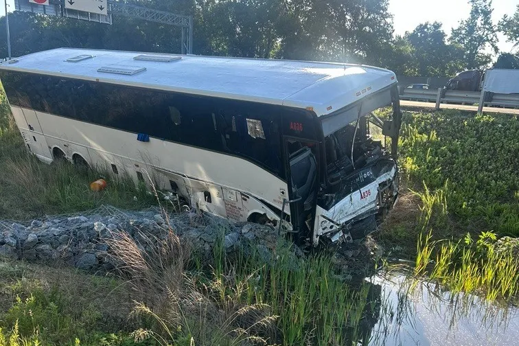 A damaged passenger bus in a ditch on the side of a highway after a fatal accident.
