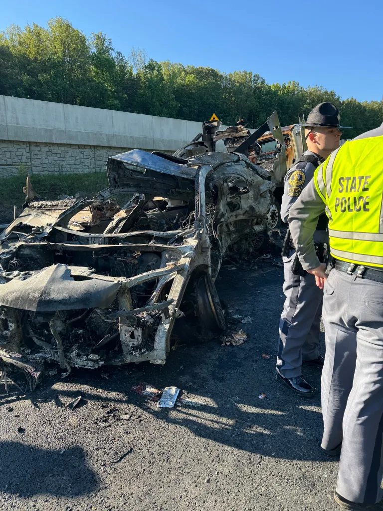 Virginia State Police at the scene of a fatal bus crash on I-95 near Quantico, with the charred remains of a vehicle in the foreground.