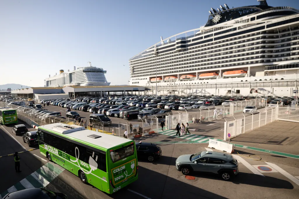 An electric bus driving past the MSC World Europa cruise ship at the Grand Port Maritime de Marseille.