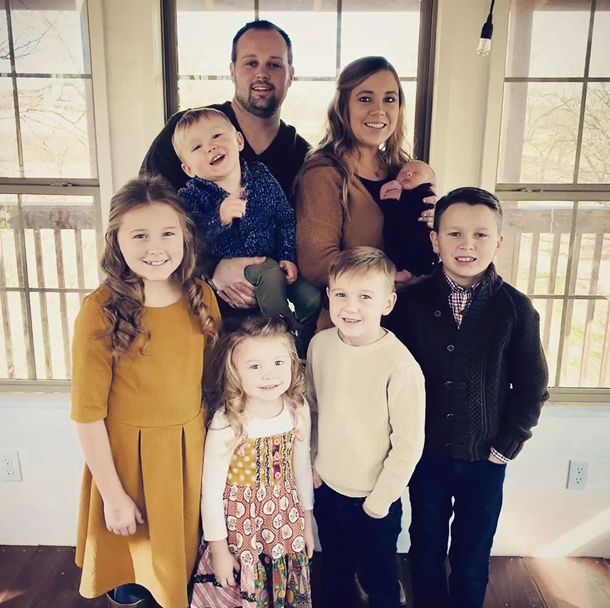 The Duggar family poses together, with the parents standing in the back holding two of their children, and four other children standing in front.