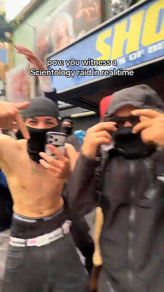 Two young men wearing balaclavas with their hands in gang signs, one topless, filming themselves.