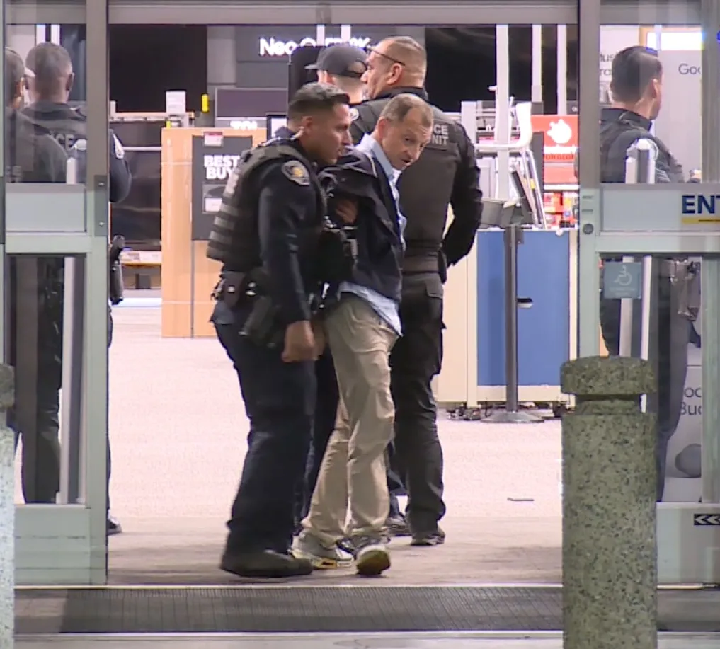 Police officers escort a man out of a Best Buy store.