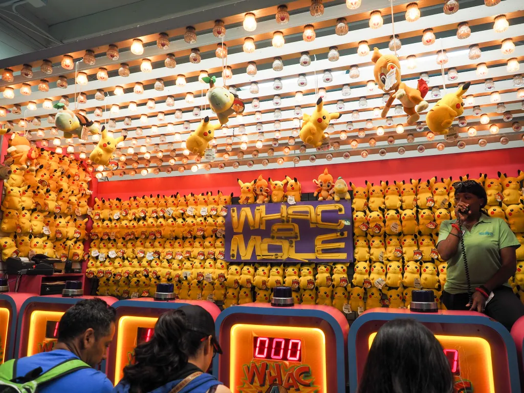 People playing Whac-A-Mole at an arcade with a wall of Pikachu plush toys.