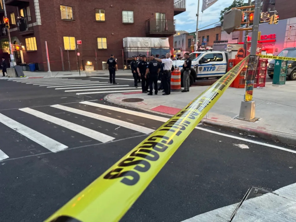 Police tape blocking a street with officers and an NYPD vehicle in the background.