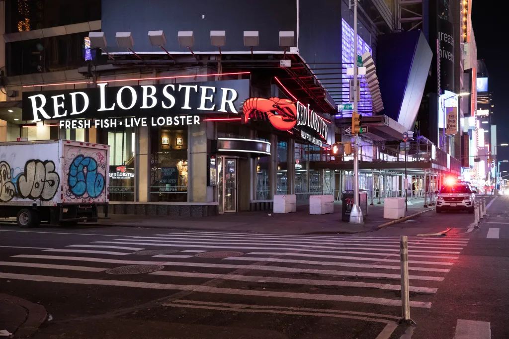 A police car with flashing lights parked in front of a Red Lobster restaurant at night.