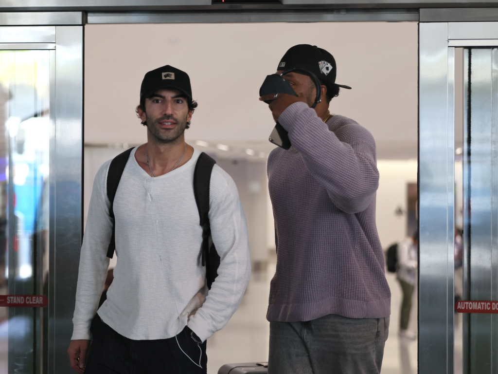 Justin Baldoni in a white shirt and black cap at LAX.