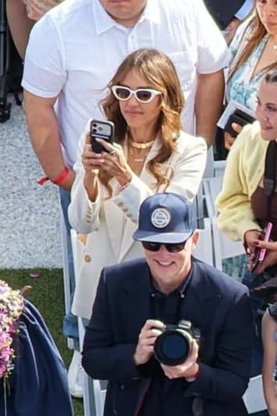 Jessica Alba recording the graduation with her phone while Cash Warren smiles, holding a camera.