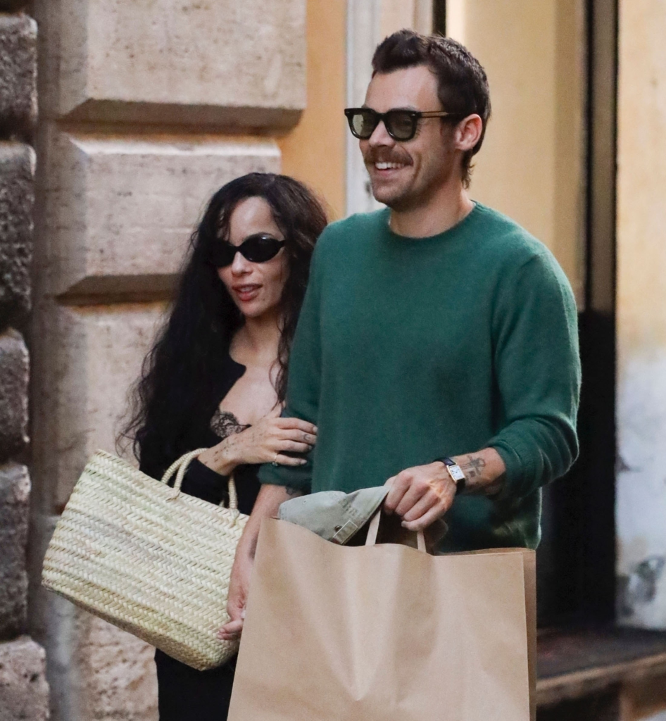 Harry Styles, in a green sweater and Zoe Kravitz, in a black dress and cardigan, walking and holding shopping bags in Rome.