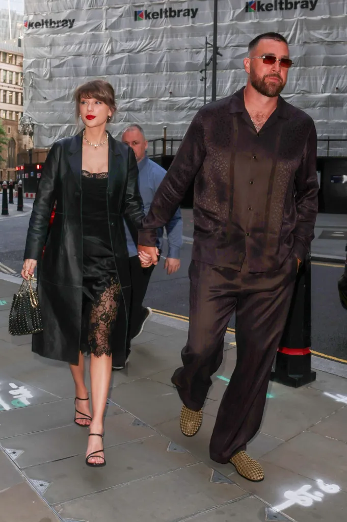 Taylor Swift in a black lace dress and leather coat holding hands with Travis Kelce in a dark patterned shirt and pants.
