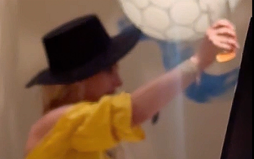 Britney Spears, in a black hat and yellow top, raising a glass while appearing unsteady.