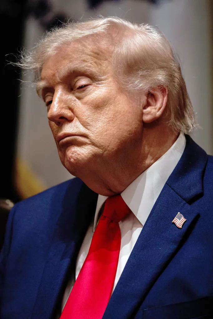 Close-up of President Donald Trump in a blue suit with a red tie and an American flag pin.