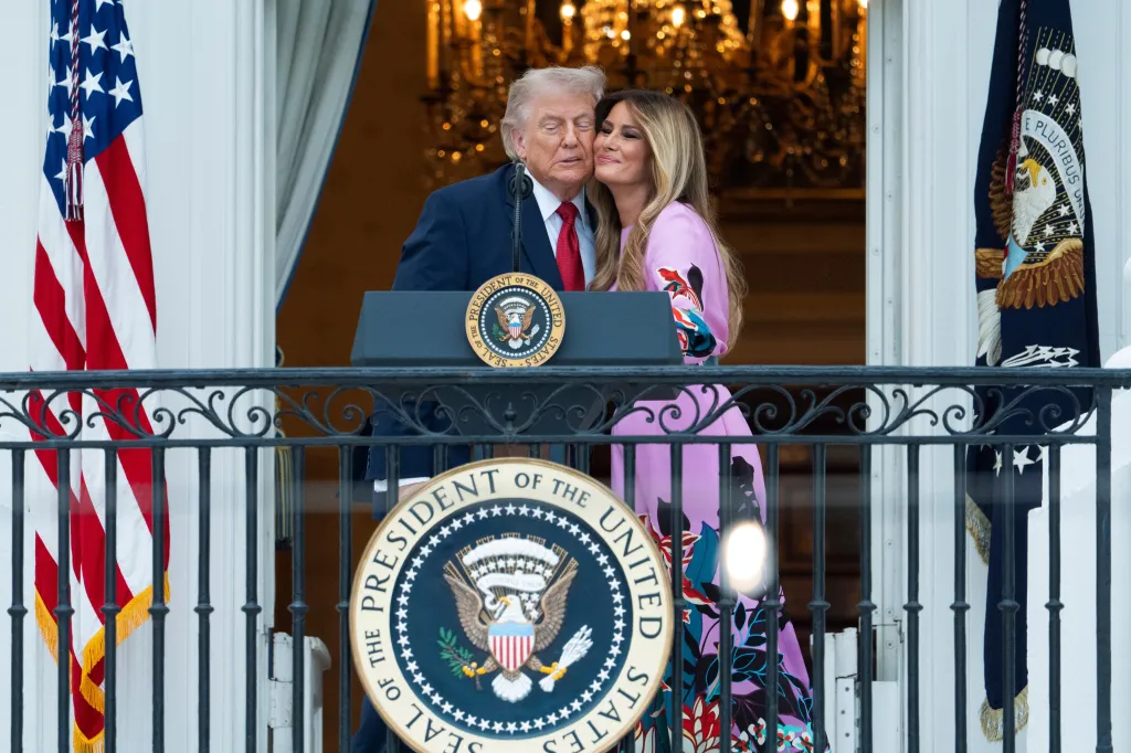 President Donald Trump and First Lady Melania Trump kiss as they greet attendees from the Blue Room Balcony of the White House.