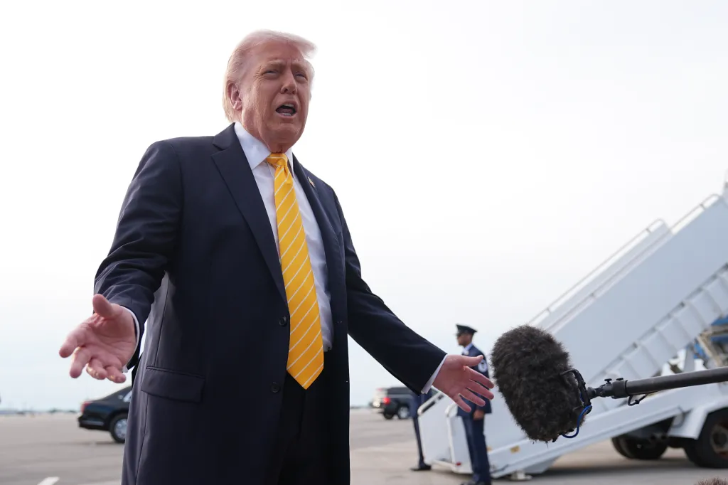 President Donald Trump speaks to reporters with his hands open and a microphone in front of him before boarding Air Force One.