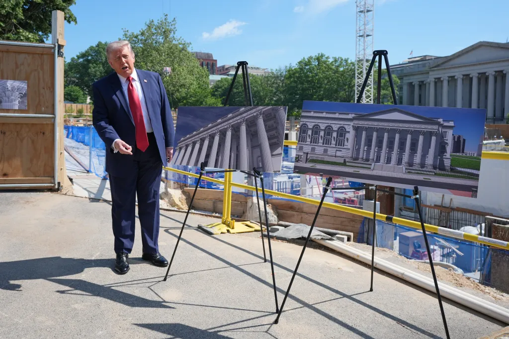 President Donald Trump stands next to large images of building renderings at a construction site.