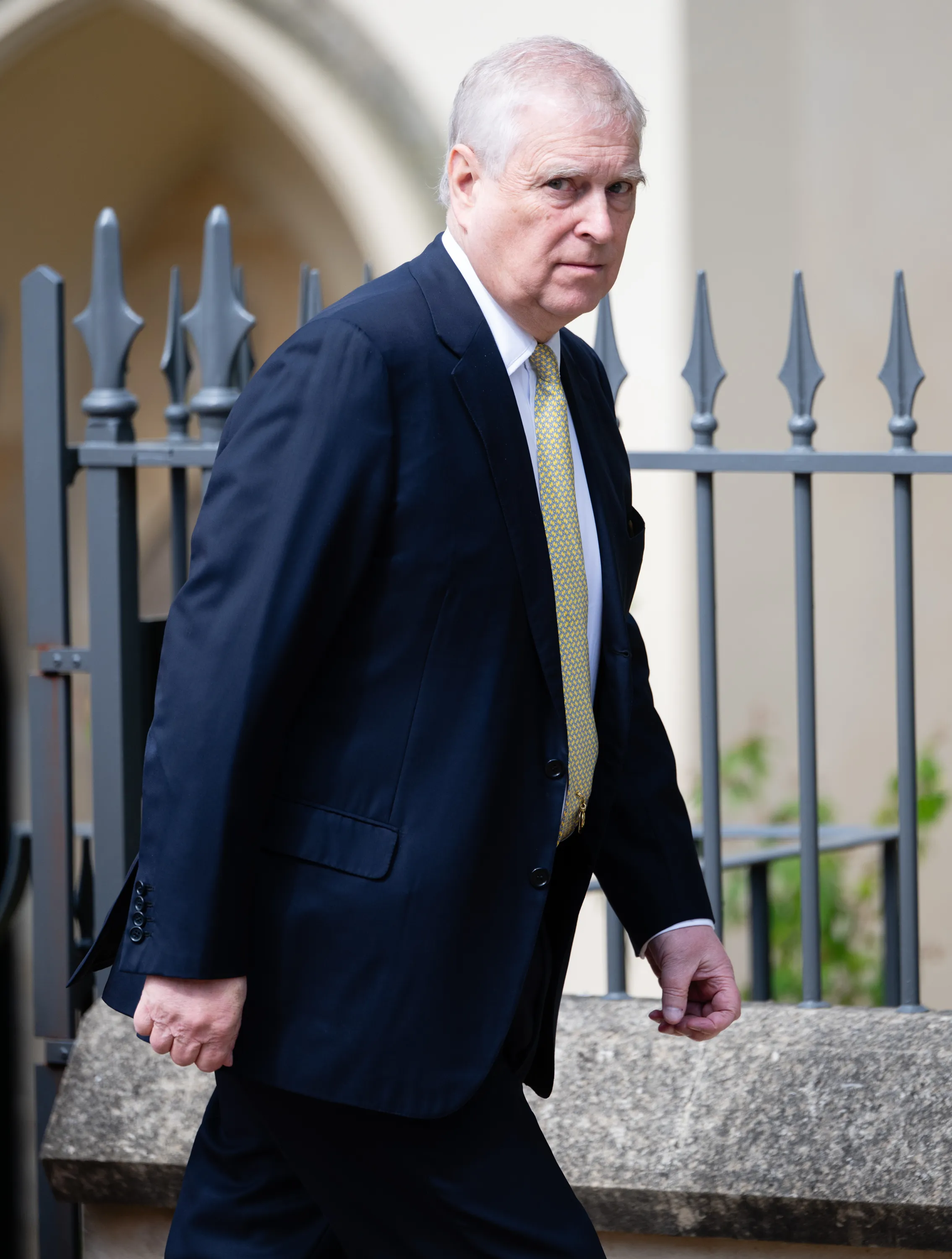 Prince Andrew, Duke of York, walking in a dark suit and patterned yellow tie.