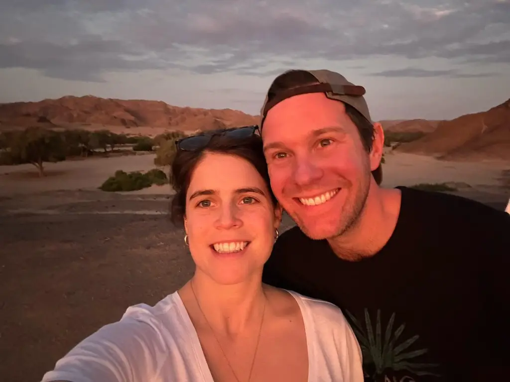 Princess Eugenie and Jack Brooksbank smiling together in a desert landscape at sunset.