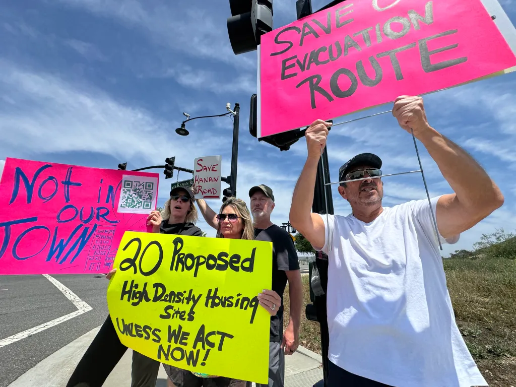 Protesters in Agoura Hills hold signs opposing a state housing plan, with messages including 