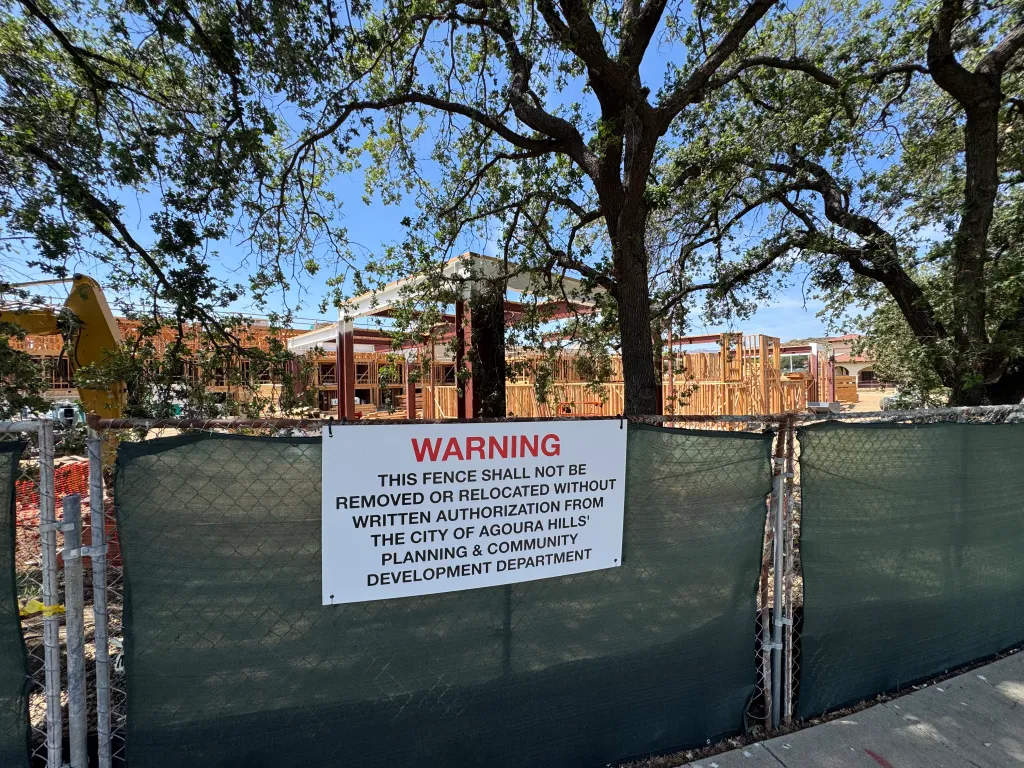 New housing units under construction on Kanan Road in Agoura Hills, as seen through a fence with a warning sign.