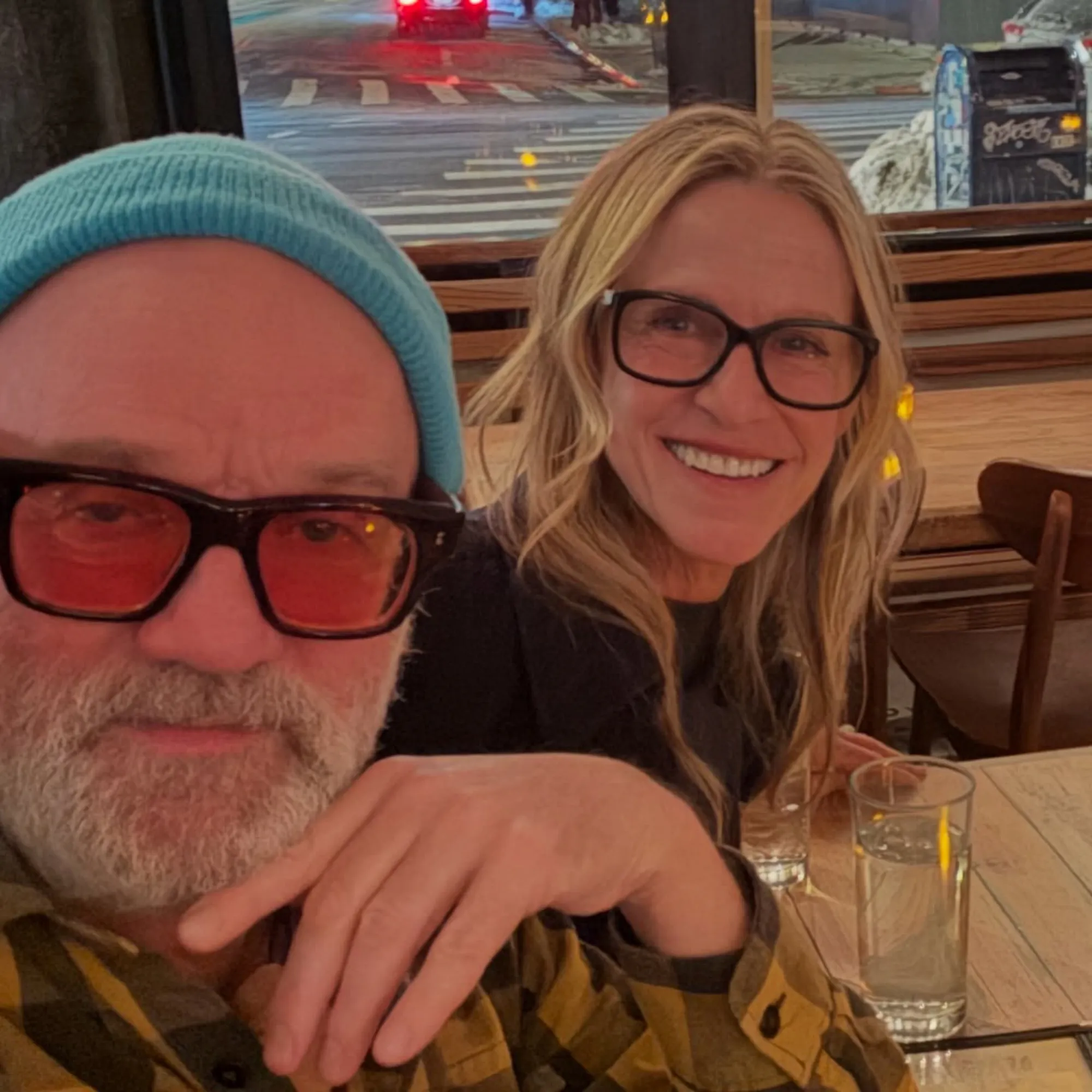 A man in a blue beanie and red-tinted glasses with a woman in black glasses.