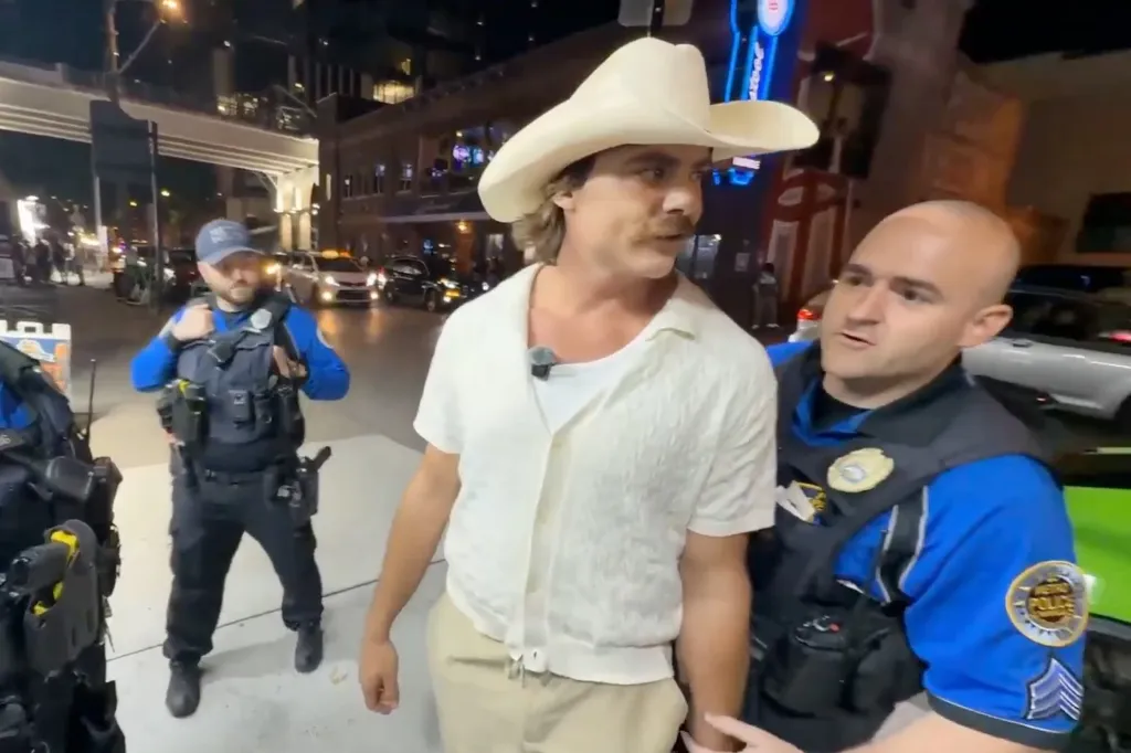 Man in a cowboy hat being arrested by police officers.
