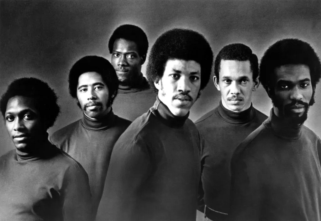 Black and white photo of R&B group The Commodores in turtle neck shirts, with Lionel Richie in the center.