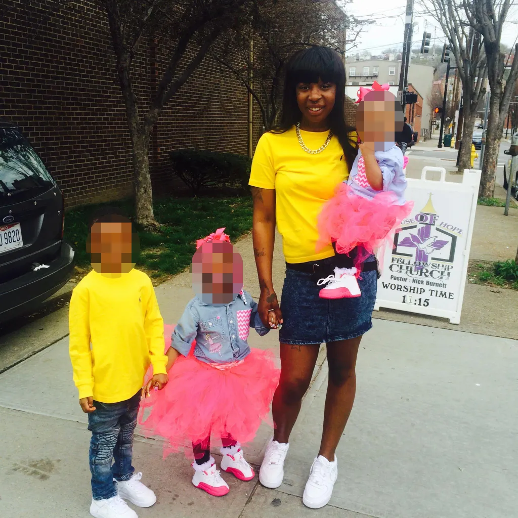 Rayshawna Deanna Dowdell with her three children, standing on a sidewalk in front of a church sign.