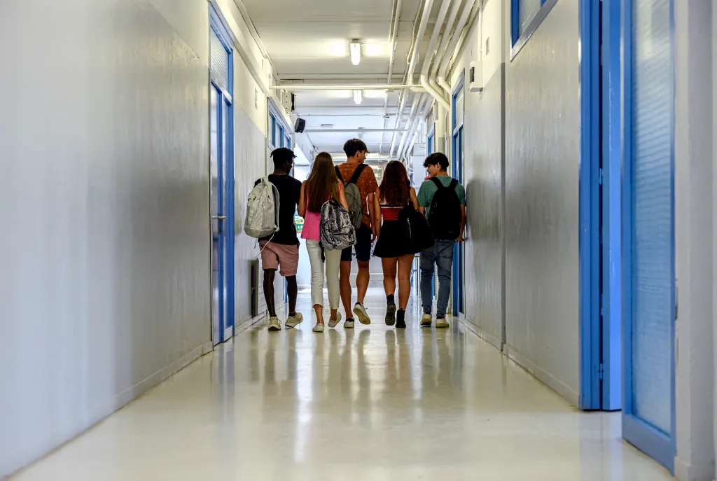 Rear view of a multiracial group of students walking in a school corridor.