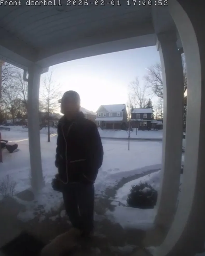 Max Miller stands on a snow-covered porch with a dog by his feet, captured by a doorbell camera.