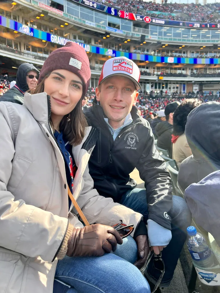 A man in a Cleveland Indians cap and a woman in a knit cap sit together in a baseball stadium.