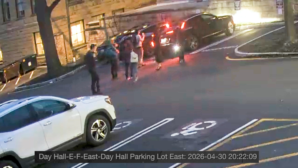 CCTV footage of people gathered around a dark SUV in a parking lot at night.