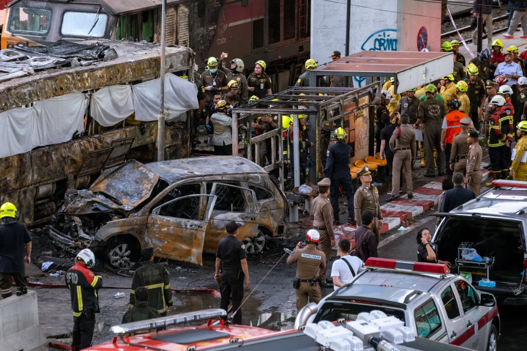 Rescue teams and firefighters at the scene of a collision between a freight train and a bus, with a burned car in the foreground.