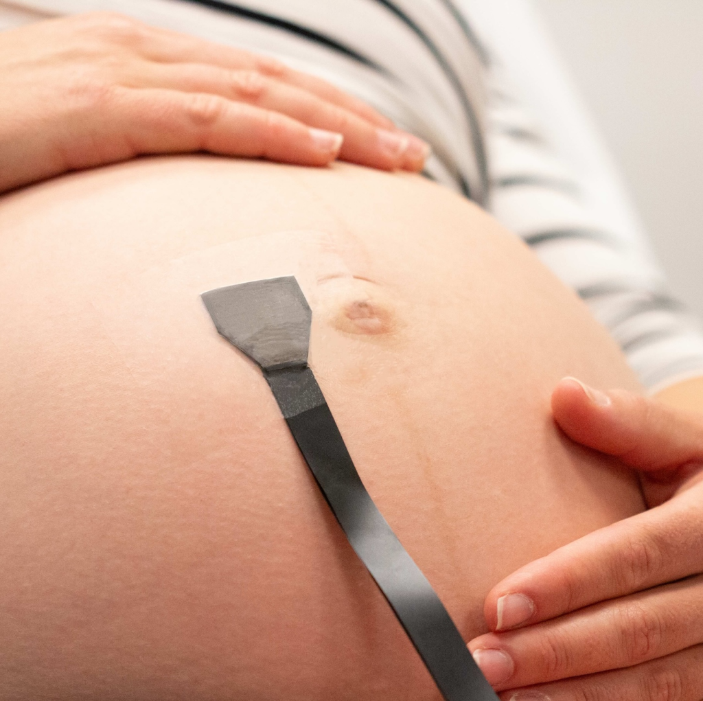 A pregnant woman wearing a monitoring patch on her belly.