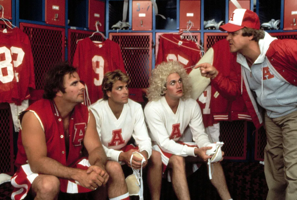 Football coach Donald Gibb speaking to Ted McGinley and Matt Salinger (in a blonde wig) in a locker room.
