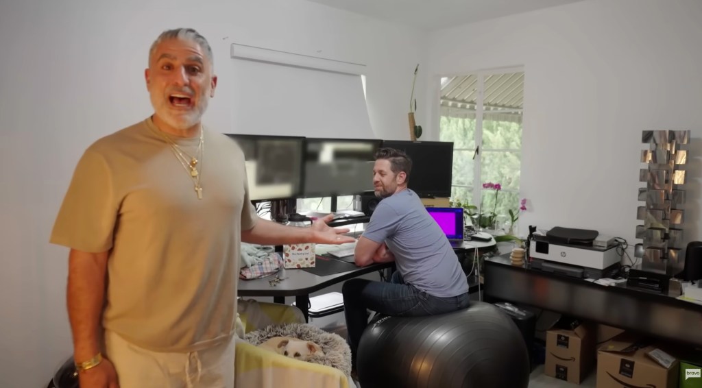 Reza Farahan gesturing toward a man sitting at a computer desk on a yoga ball.