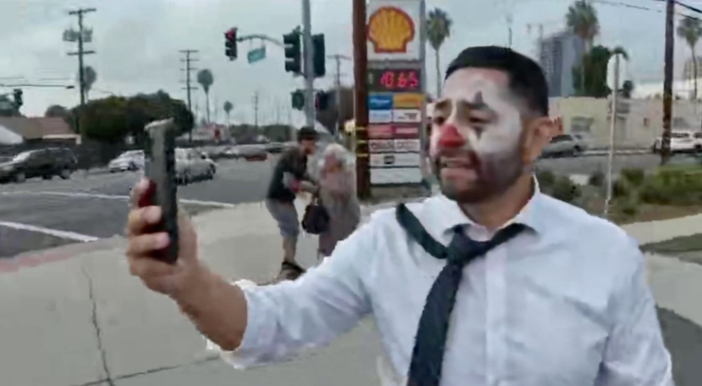 Ricardo Valencia with clown makeup recording with his phone on the street.