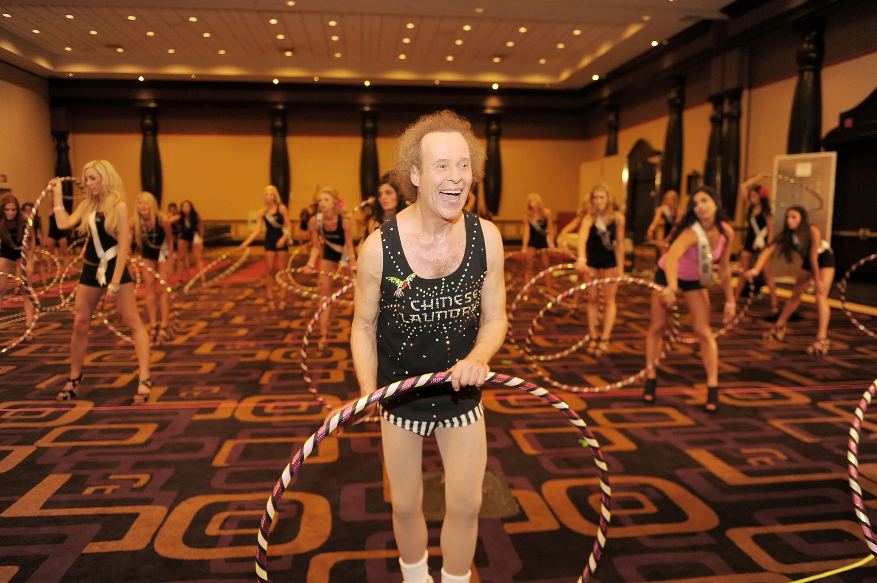 Richard Simmons hula-hooping with several beauty pageant contestants.