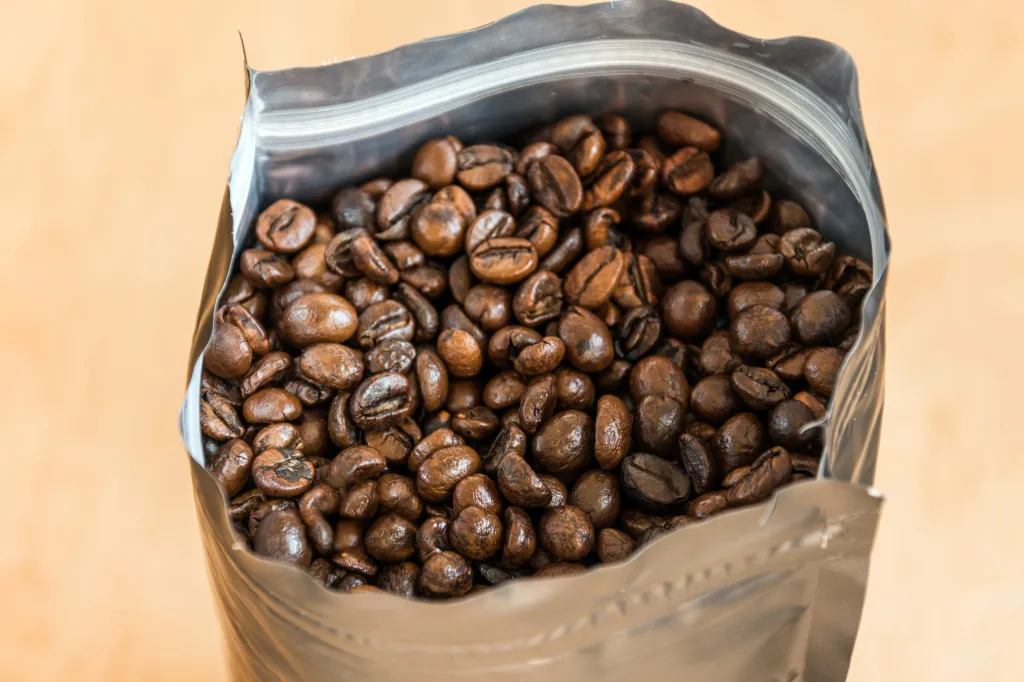 Roasted coffee beans in an open silver foil package.